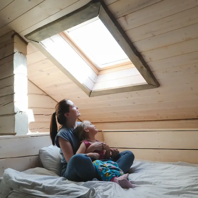 Madre e hija mirando por la ventana en un ático sentadas en la cama