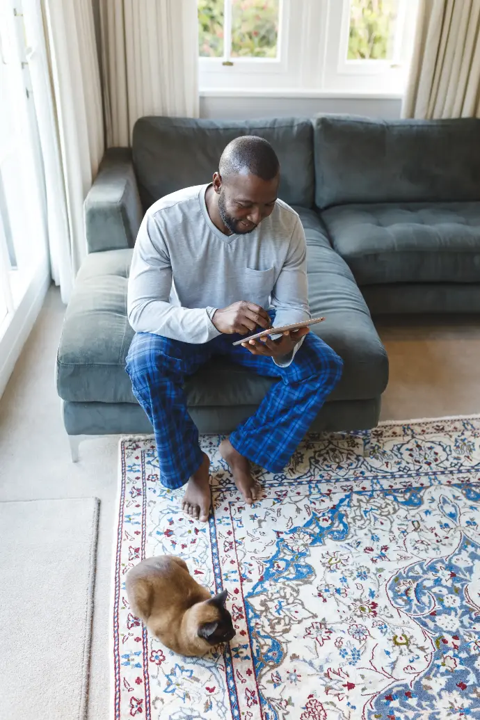 Hombre afroamericano sentado en el sillón con un ipad y un gato en el suelo
